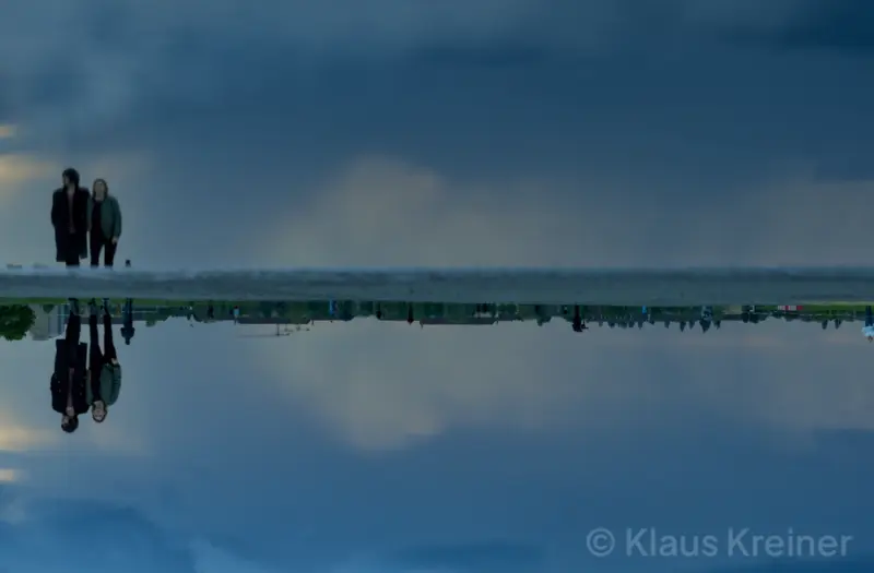 Ende Mai 2021 in Berlin: Ein Pärchen bei einem Spaziergang über das Tempelhofer Feld, aufgenommen über eine reflektierende Pfütze.