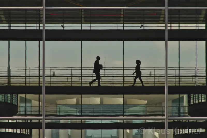 Mitte April 2019 in Berlin: Menschen begegnen sich als Silhouetten hinter einer Glasfront zwischen zwei Bürobereichen im Parlamentsviertel.