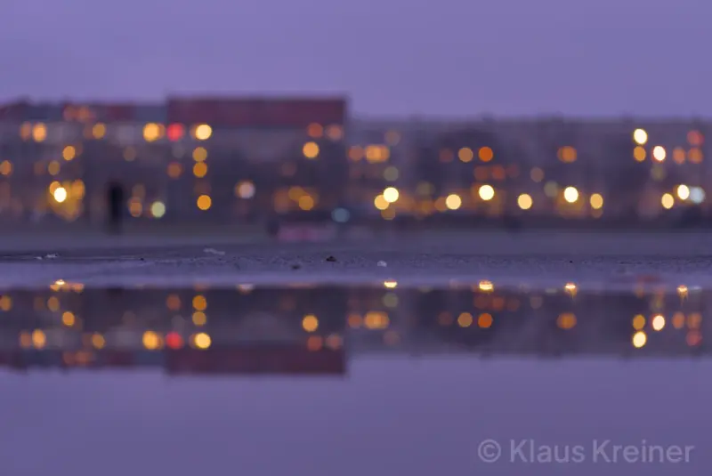 Mitte Dezember 2018 in Berlin: Reflexionen einiger beleuchteter Mehrfamilienhäuser in der Oderstraße auf der Oberfläche einer Regenpfütze.