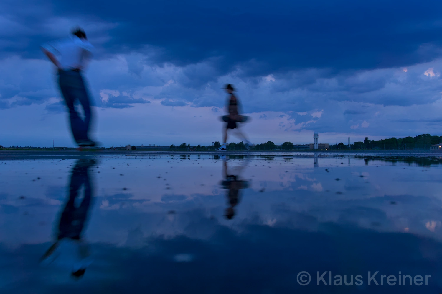 Anfang Juni 2019 in Berlin: Zwei Skater während der blauen Stunde im Spiegelbild einer Wasserfläche auf dem Tempelhofer Feld.