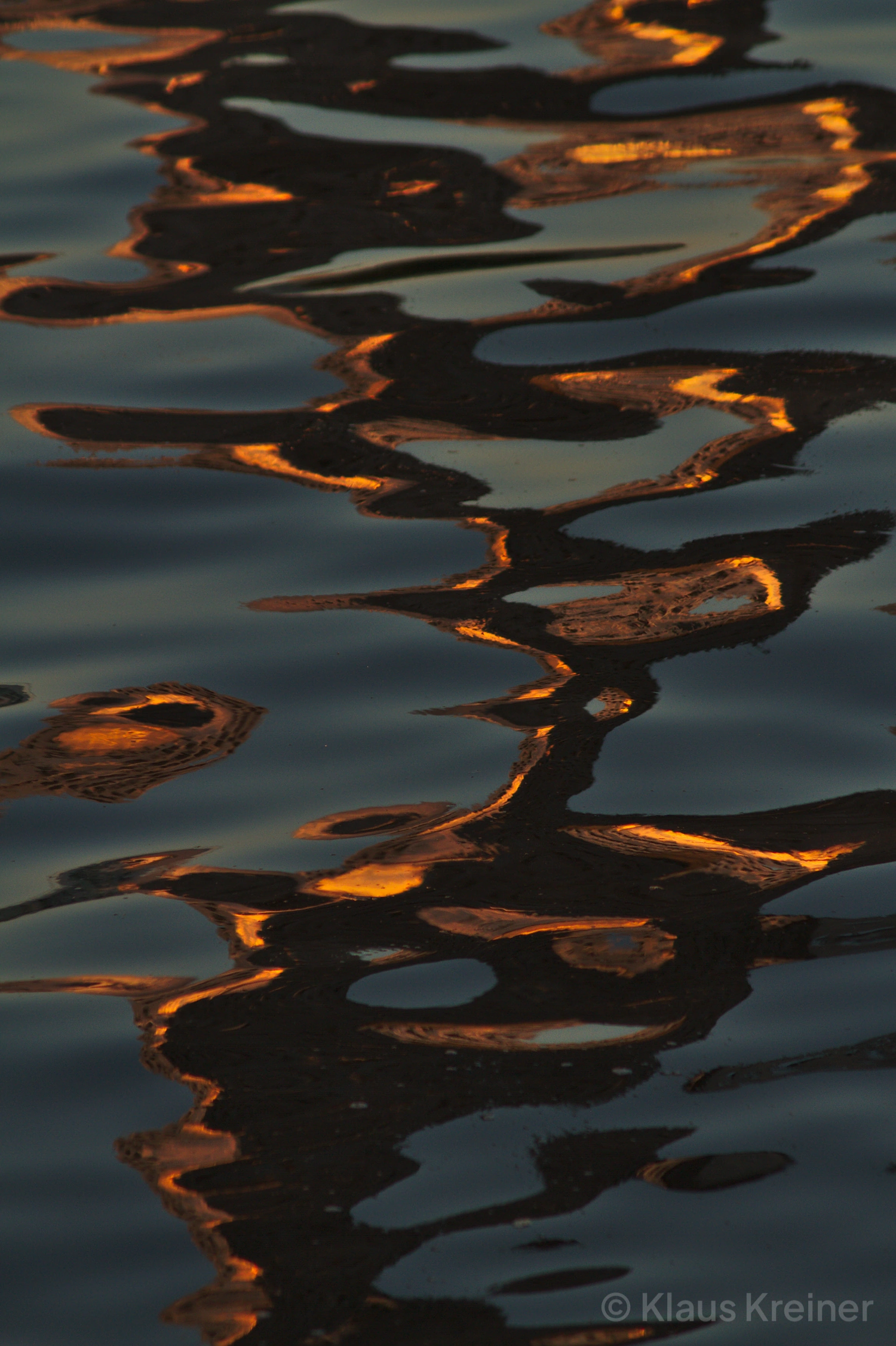 Ende Juli 2019 in Berlin: Die deformierte Spiegelung der Molecule-Man-Skulptur auf der Wasseroberfläche von Berlin-Treptow.