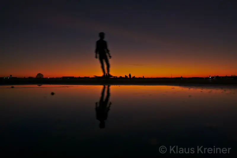 Mitte Februar 2019 in Berlin: Im Spiegelbild einer Wasserfläche gleitet ein Skater auf dem Tempelhofer Feld durch das Abendrot.