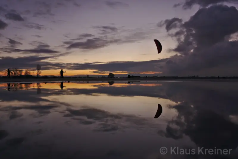 Mitte Dezember 2018 in Berlin: Ein Kiter und sein Segel vor den Abendrotfarben im Spiegelbild einer Wasserfläche.