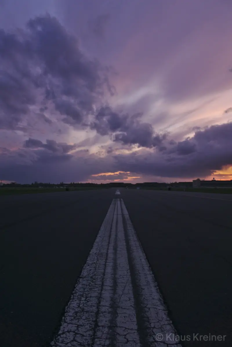Mitte April 2017 in Berlin: Der markierte Mittelstreifen der Rollbahn vom Flughafen Tempelhof führt in ein lilafarbenes Wolkenbild am Abend.