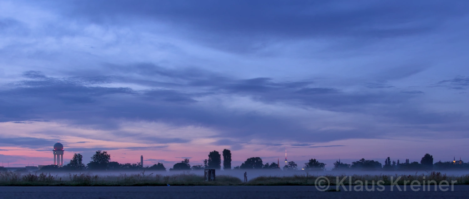 Anfang August 2019 in Berlin: Panorama-Ansicht vom Tempelhofer Feld im Abendrot, im Hintergund mit Radar- und Fernsehturm im Nebel.