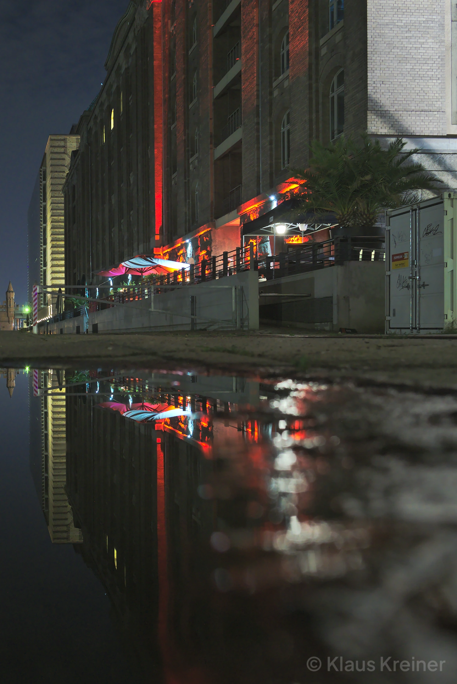 Ende Oktober 2019 in Berlin: Eine Pfützen-Spiegelung mit Neon-Licht am Abend vom Spreespeicher über Universal zur Oberbaumbrücke.