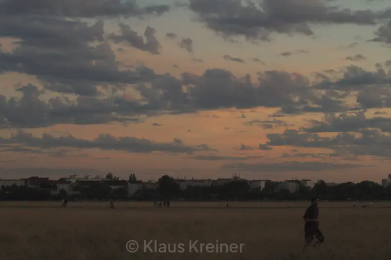 Anfang August 2016 in Berlin: Ein Jogger läuft an einem sommerlichen Abend über das Tempelhofer Feld, im Hintergrund wird flaniert.
