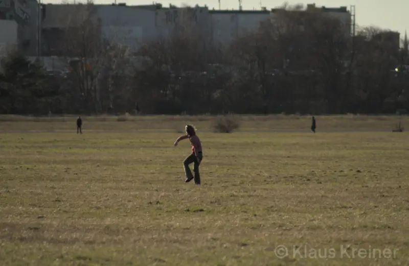 Mitte März 2023 in Berlin: Eine Person tanzt freestylish auf einem Feld, im Hintergrund ist die Skyline vom Bezirk Tempelhof zu sehen.