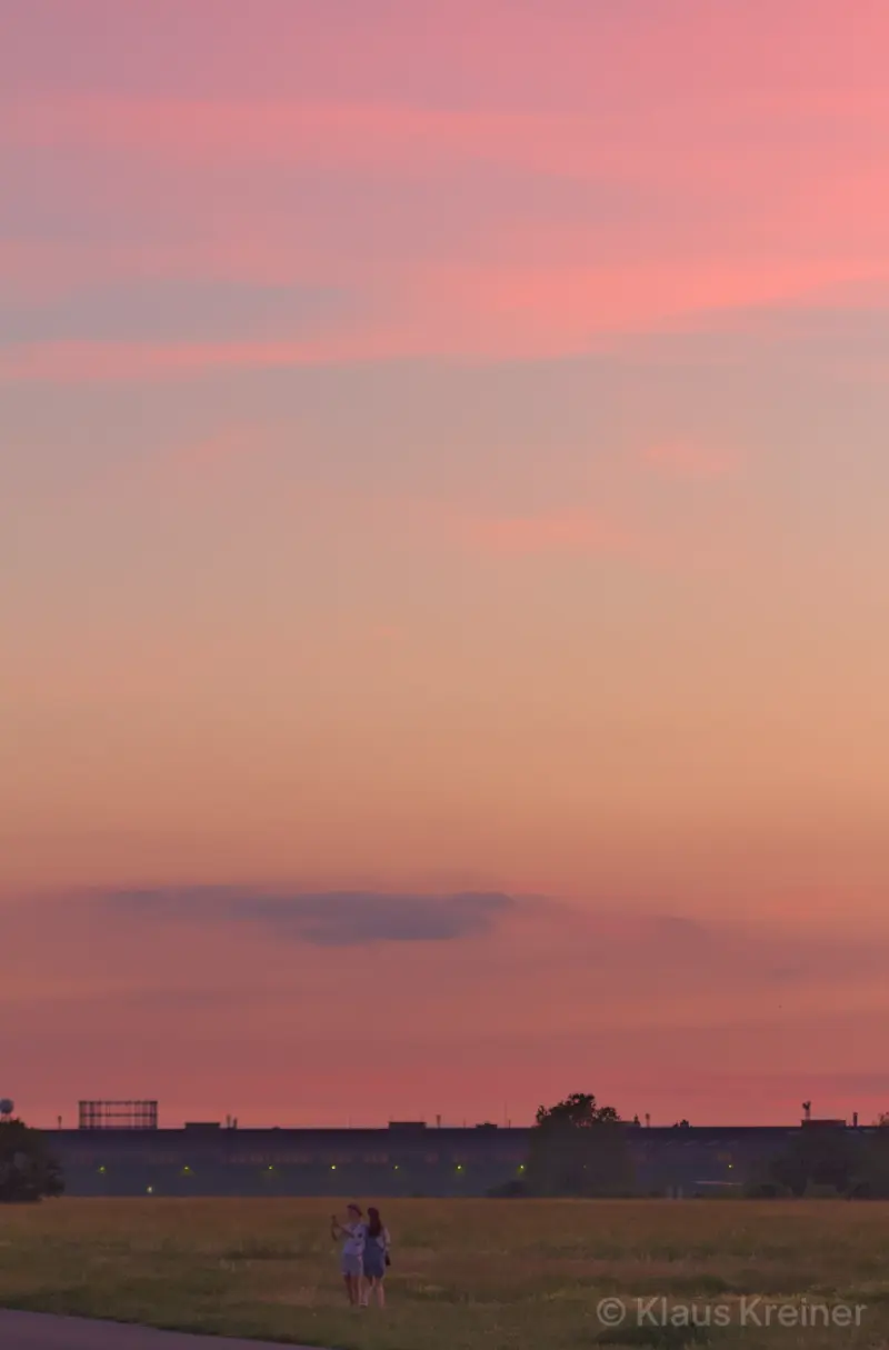 Mitte Juni 2019 in Berlin: Menschen auf dem Feld sowie im Hintergrund das ehemalige Flughafengebäude im sommerlichen Abendrot.
