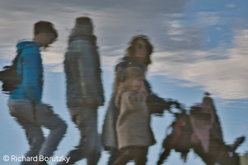 Anfang Oktober 2023 in Berlin: Eine Kleinfamilie auf dem Tempelhofer Feld wird unscharf auf einer Wasseroberfläche gespiegelt.