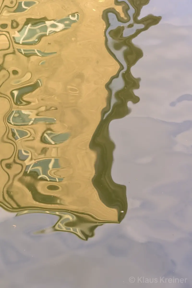 Ein Wohnhaus spiegelt sich verzerrt an der Wasseroberfläche