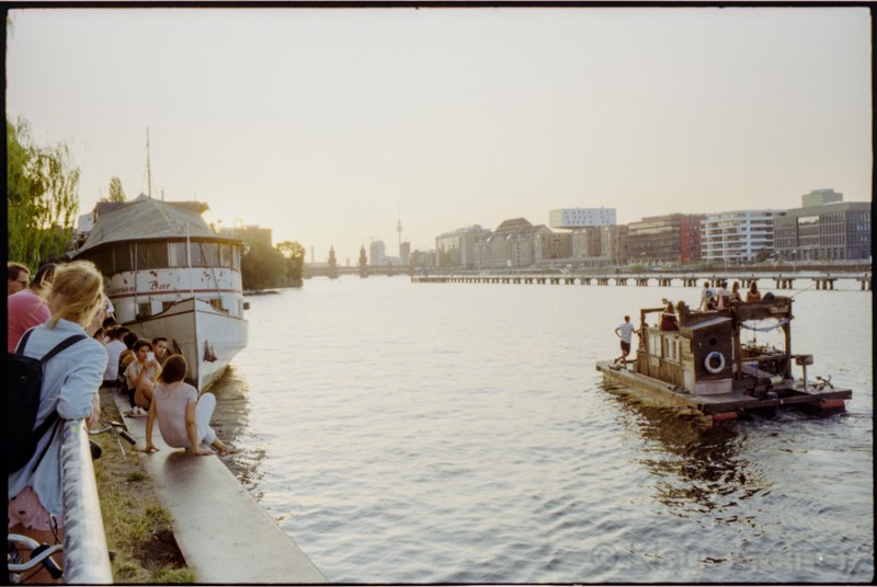 Junge Leute verweilen an einem Sommerabend nahe der MS Hoppetosse am Spreeufer.