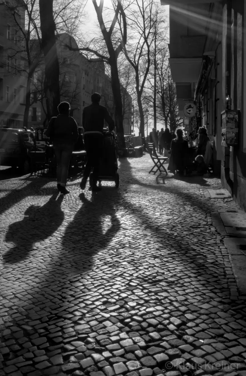 Flanierende Menschen mit Kinderwagen im Schillerkiez bei Gegenlicht