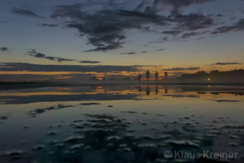 Menschen laufen im Abendrot durch den Nebel und spiegeln sich im Wasser